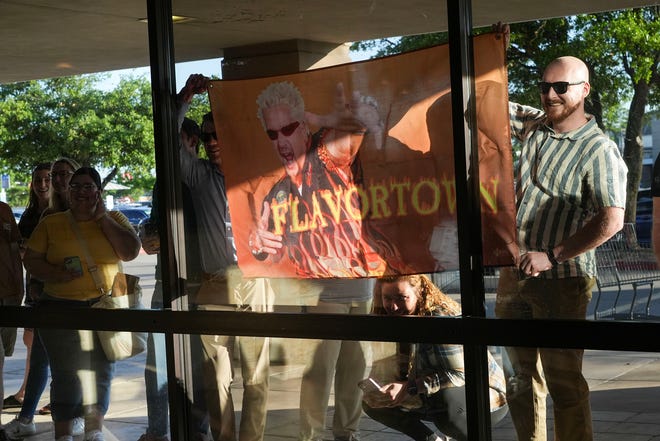 Van Heye and Brenton Novit hold up a sign through the window at Guy Fieri during his meet-and-greet at Twins Liquor at the Hancock Center on Thursday, March 28, 2024. Fieri came to Texas in support of his and Sammy Hagar’s Santo Spirits brand.